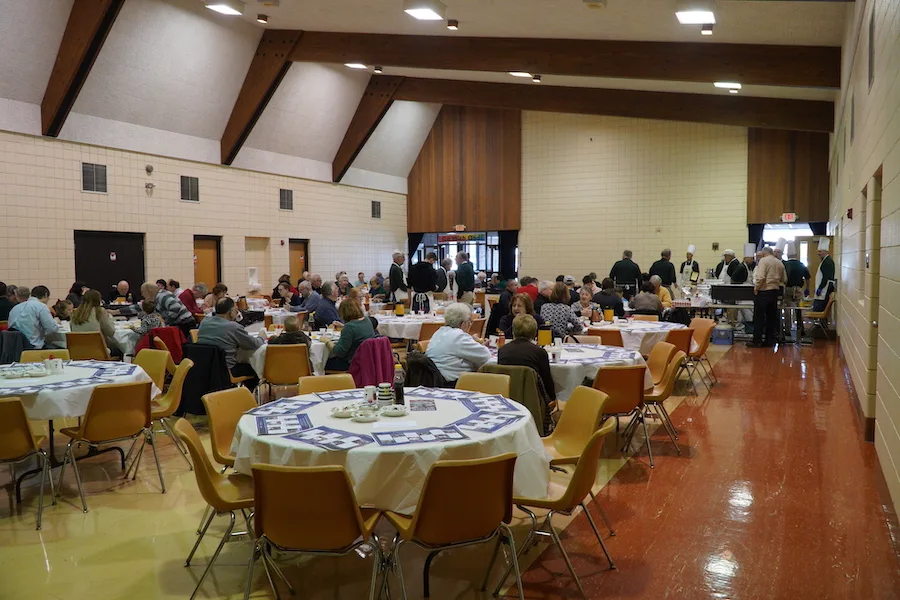 The parish hall set with round tables as guests are served breakfast