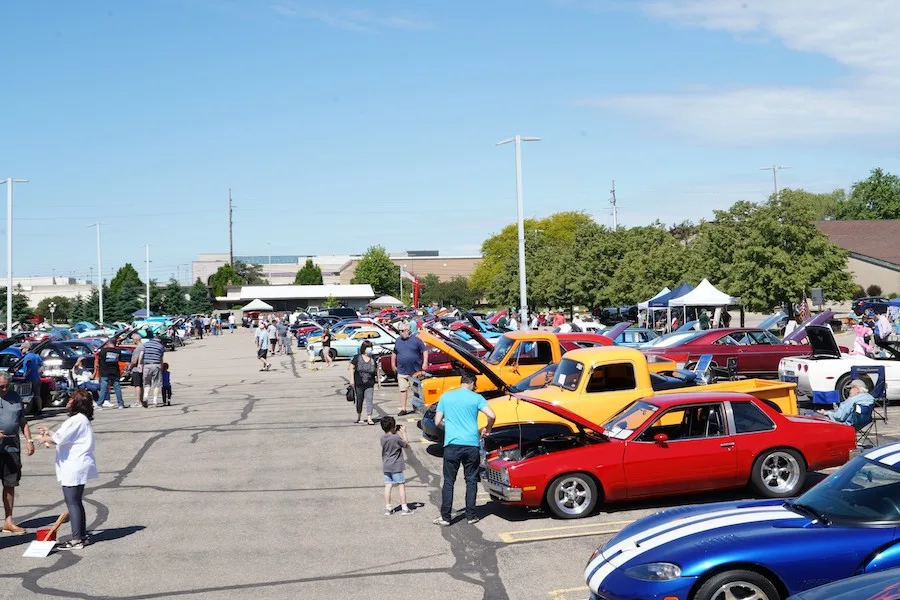 Rows of classic cars with hoods raised at the council car show, visitors walking between them