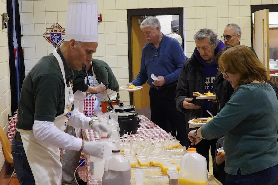A council member in a chef's hat serving juice to parishioners in the buffet line