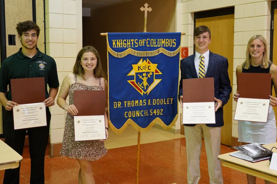 Four scholarship recipients holding award folders beside the Dr. Thomas A. Dooley Council 5492 banner
