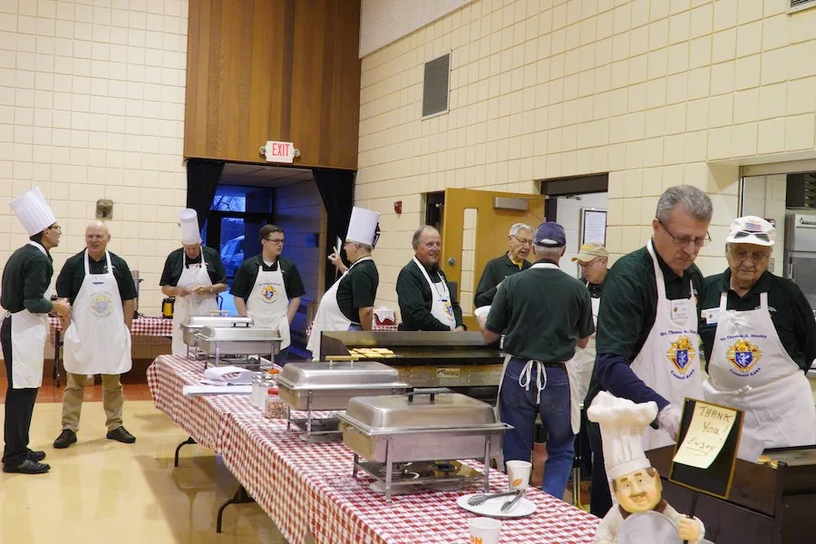 Council 5492 members in chef hats and aprons behind the serving line at a parish dinner